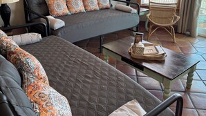 A cozy living room with a sofa, a chair, and a small table. There are framed pictures on the wall and a window with blinds. - Beach Front Sleeps 10 Walking distance to everything (St. George Island)