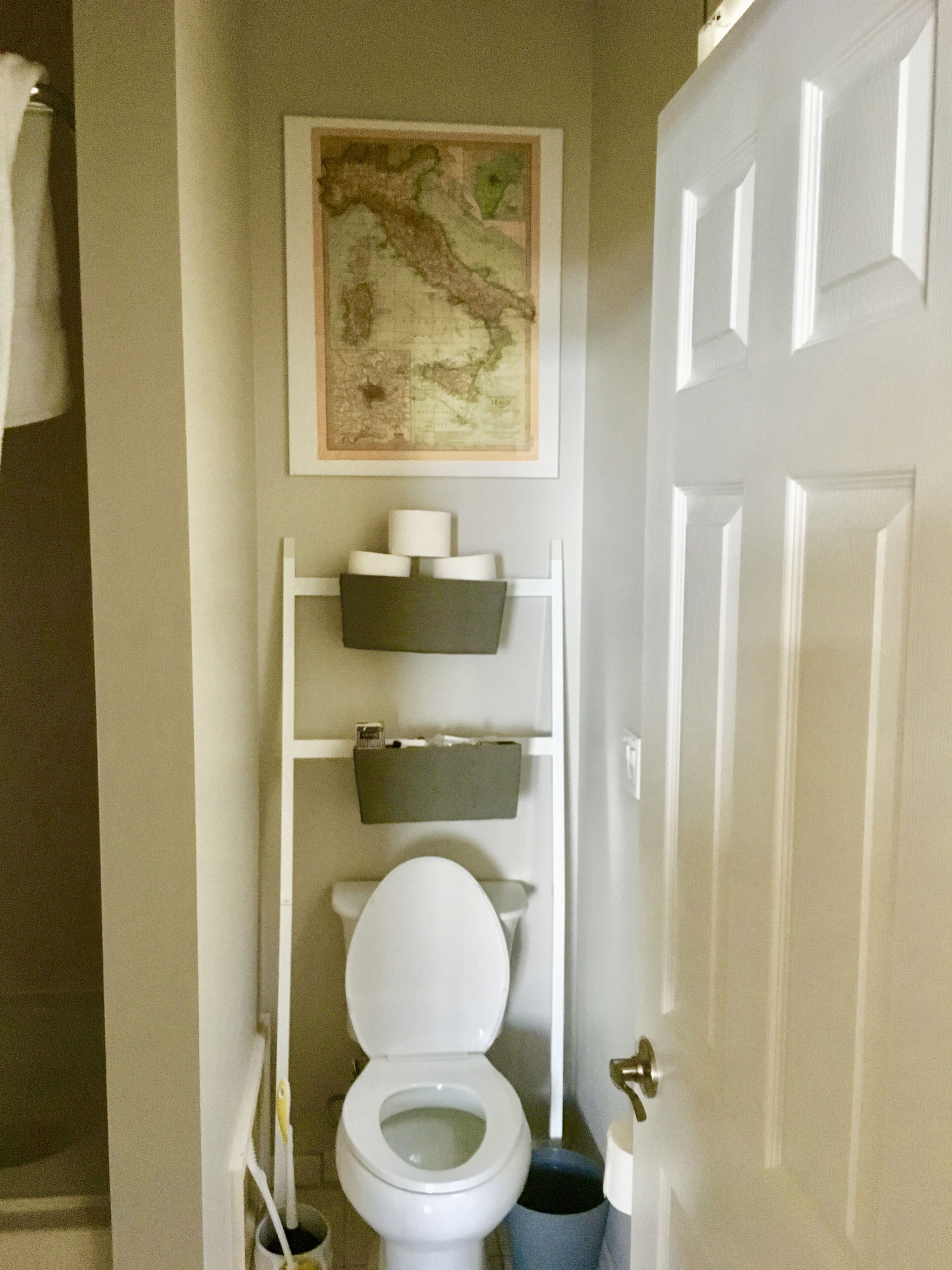 A bathroom with a toilet, a shelf with toiletries, and a map on the wall.
