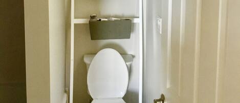 A bathroom with a toilet, a shelf with toiletries, and a map on the wall.