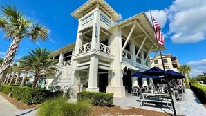 A two-story building with a balcony, palm trees, and an American flag. - Walk to Beach or Pool-2 Bikes/Match Pointe CH (Santa Rosa Beach)