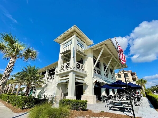 A two-story building with a balcony, palm trees, and an American flag.