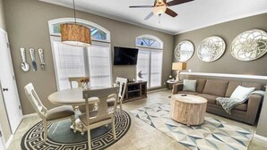 A living room with a dining table, chairs, a round coffee table, a sofa, a TV, and decorative wall art. - Walk to Beach or Pool-2 Bikes/Match Pointe CH (Santa Rosa Beach)