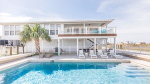A two-story house with a swimming pool, a covered patio, and a view of the ocean.