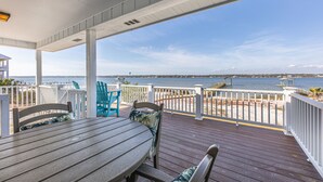 A covered outdoor deck with a table and chairs, overlooking a beach and the sea.
