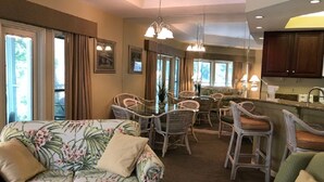 A spacious living area with a floral sofa, wicker chairs, a dining table, and a kitchen area with wooden cabinets. - STUNNING 2 BED 2 BATH SLEEPS 6 INCLUDES FREE GOLF/TENNIS WITH WESTIN AMENITIES (Hilton Head Island)