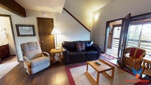 A living room with a wooden floor, a black leather sofa, a wooden armchair, a small wooden table, and a wooden chair with a red cushion. - Close to Lifts | Fireplace | Views | Ski Run B6 (Angel Fire)