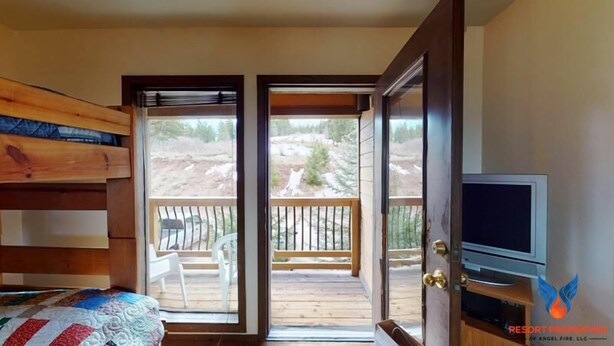 A bedroom with a wooden bunk bed, a television on a wooden stand, and a balcony with a view of a rocky landscape. - Close to Lifts | Fireplace | Views | Ski Run B6 (Angel Fire)
