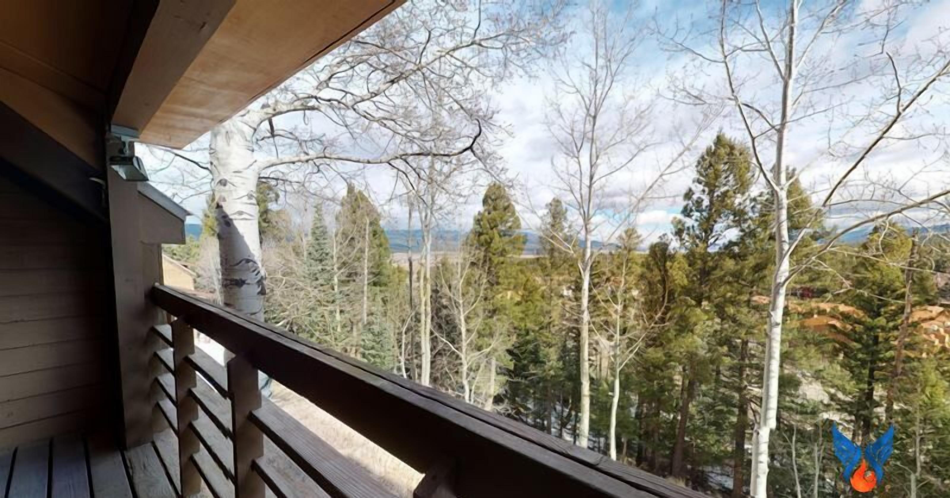 Un balcon en bois offrant une vue sur une forêt et des montagnes.