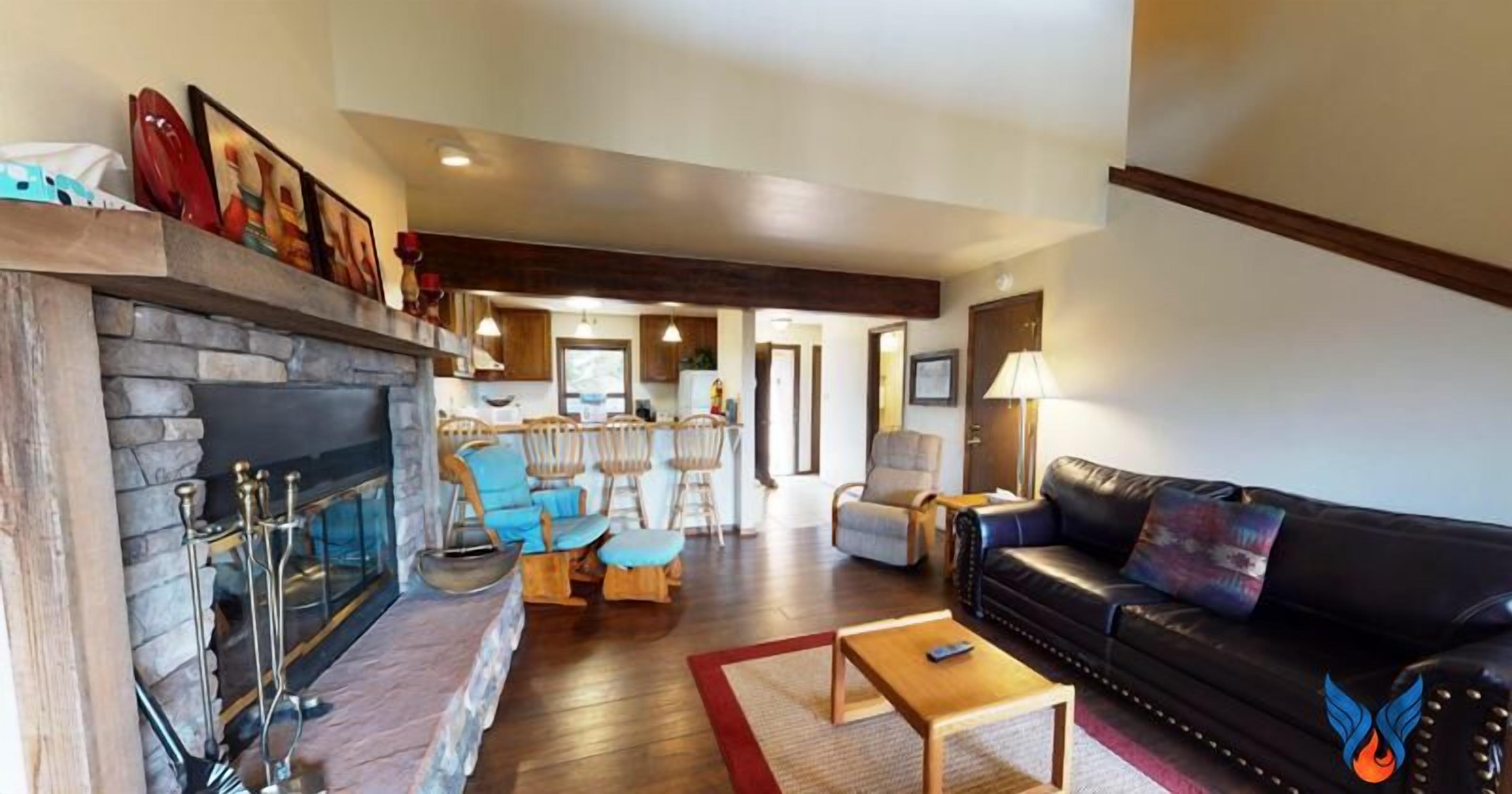 A spacious living area with a stone fireplace, leather sofa, and wooden chairs.