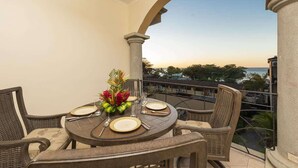 A balcony with a round table set for dining, featuring a vase of flowers and a view of the ocean and buildings in the background.