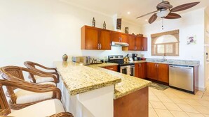 A kitchen with wooden cabinets, a granite countertop, a built-in oven, a dishwasher, and a ceiling fan.