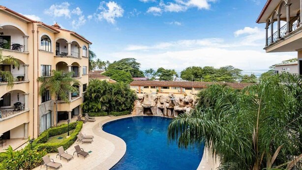 A hotel courtyard with a swimming pool, multiple balconies, and lush greenery.