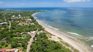 An aerial view of a coastal town with a beach, buildings, and a clear sky.