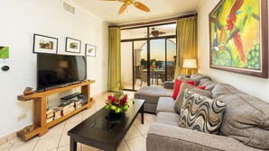 A living room with a flat-screen TV, wooden entertainment unit, grey sofa, and a ceiling fan.
