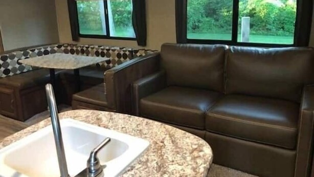Cocina compacta para camper con encimera de granito, un lavamanos y un sofá de cuero marrón.