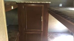 Un cuarto pequeño y cerrado con una cama litera y un mueble bajo.