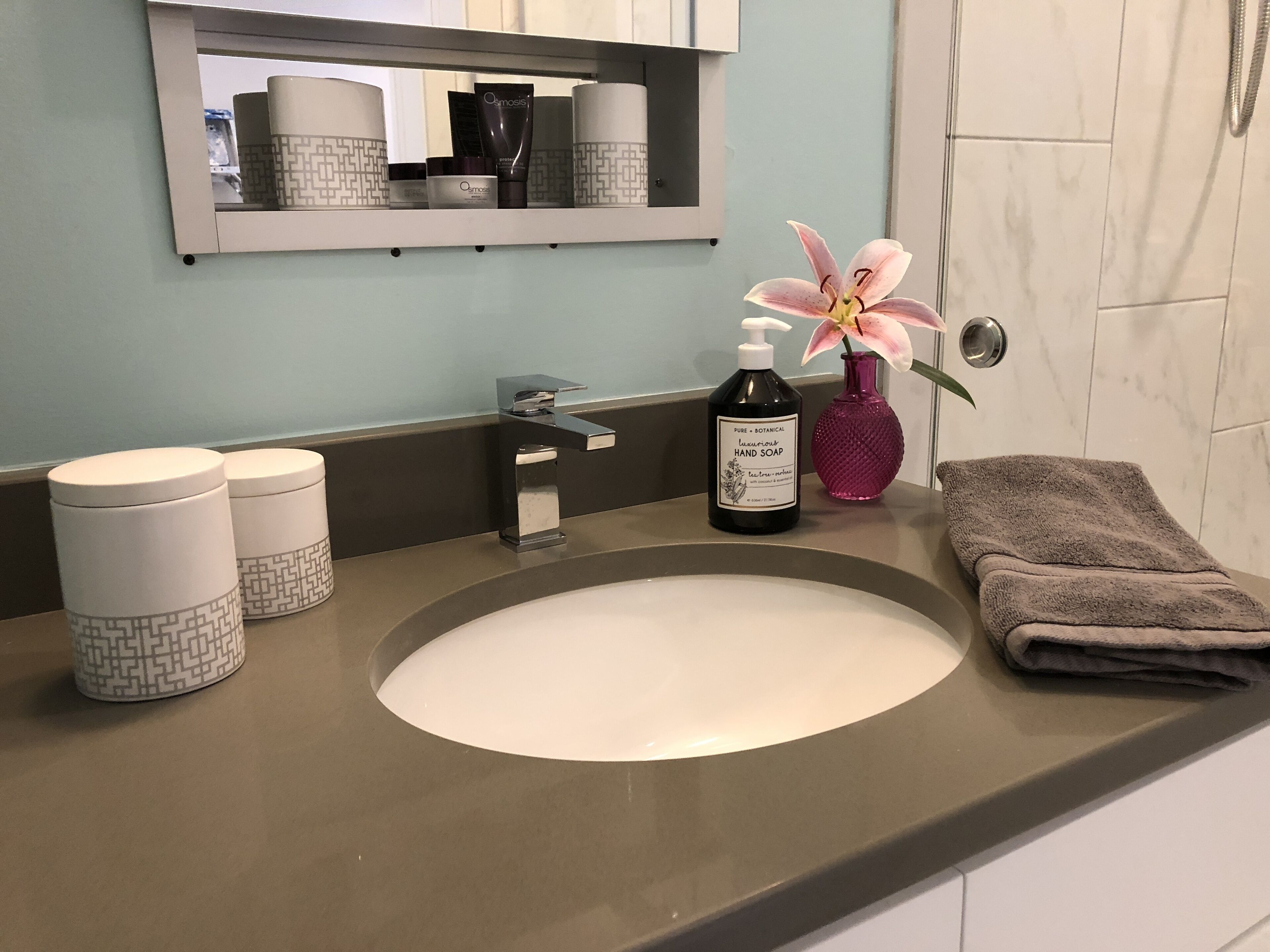 A bathroom with a sink, a mirror, toiletries, and a towel.