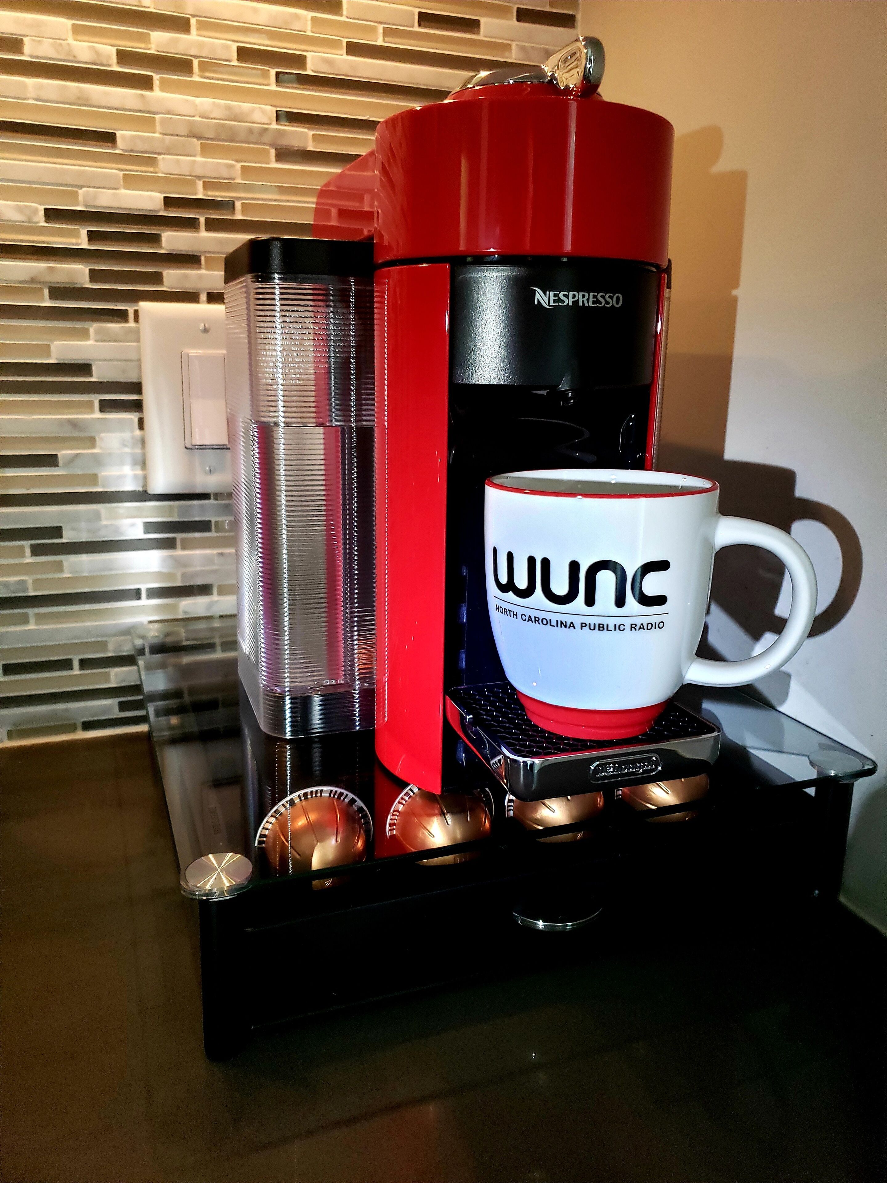 Une machine à café Nespresso avec une tasse WUNC posée sur le bac d’égouttement.