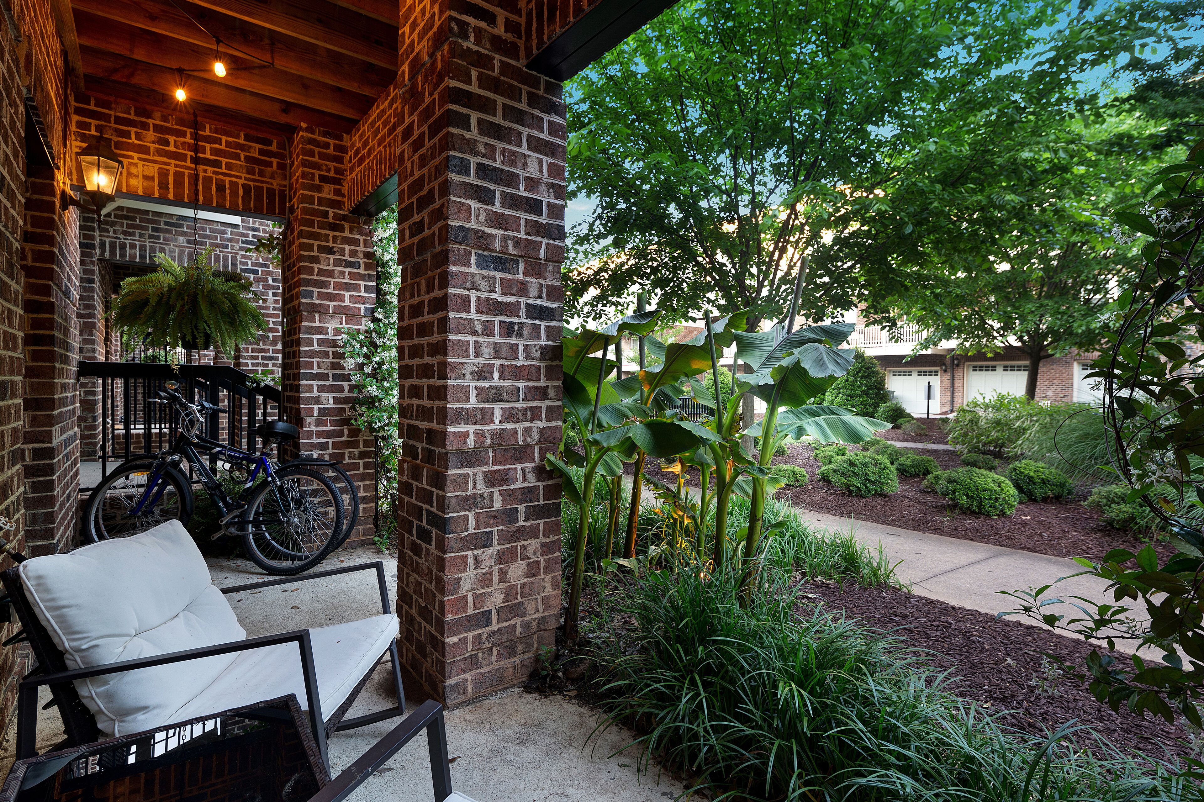 A covered patio with a brick wall, a white cushioned chair, and a bicycle.