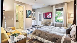 Ein Hotelzimmer mit einem großen Bett, einer Sitzecke mit Stuhl und Tisch, einer kleinen Küchenzeile und einem Badezimmer mit Dusche und Toilette.