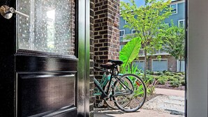 Eine Tür mit Fensterteil, ein Fahrrad, das an einer Ziegelwand angelehnt ist, und eine Fußmatte.