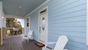 En veranda med två vita Adirondack-stolar, ett träbord och en dörr med ett glasparti.