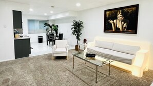 A modern living room with a white sofa, a glass coffee table, and a painting on the wall.