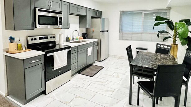 A modern kitchen with grey cabinets, a black countertop, and a marble-tiled floor.
