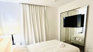 A hotel room with a bed, a mirror, a television, and a bathroom.