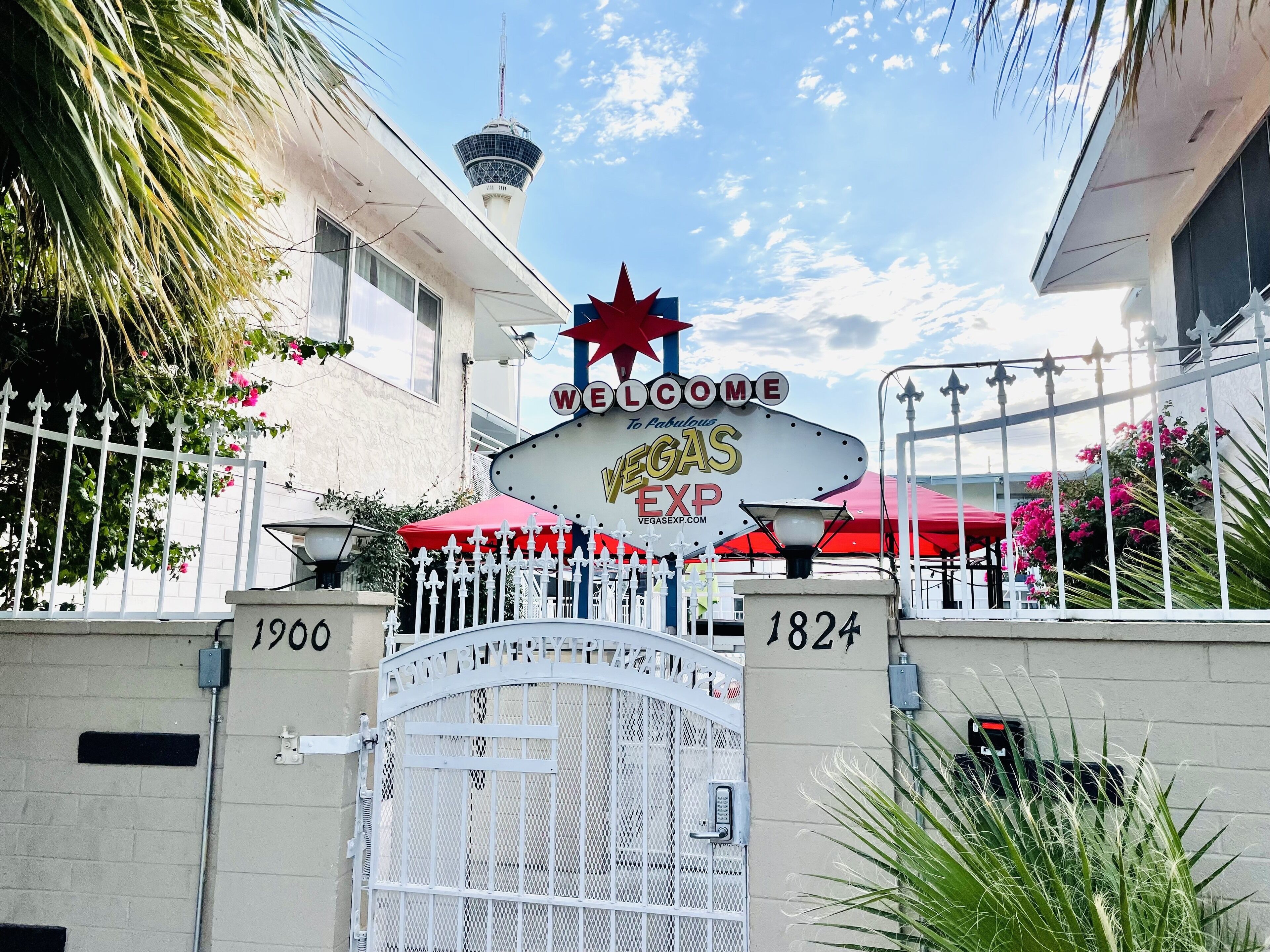 A gate with a 'Welcome to Vegas Exp' sign, a tower in the background, and a red umbrella.