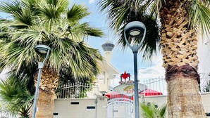 A palm tree-lined pathway leading to a building with a 'Welcome to Las Vegas' sign, a gate, and a tower-like structure in the background.