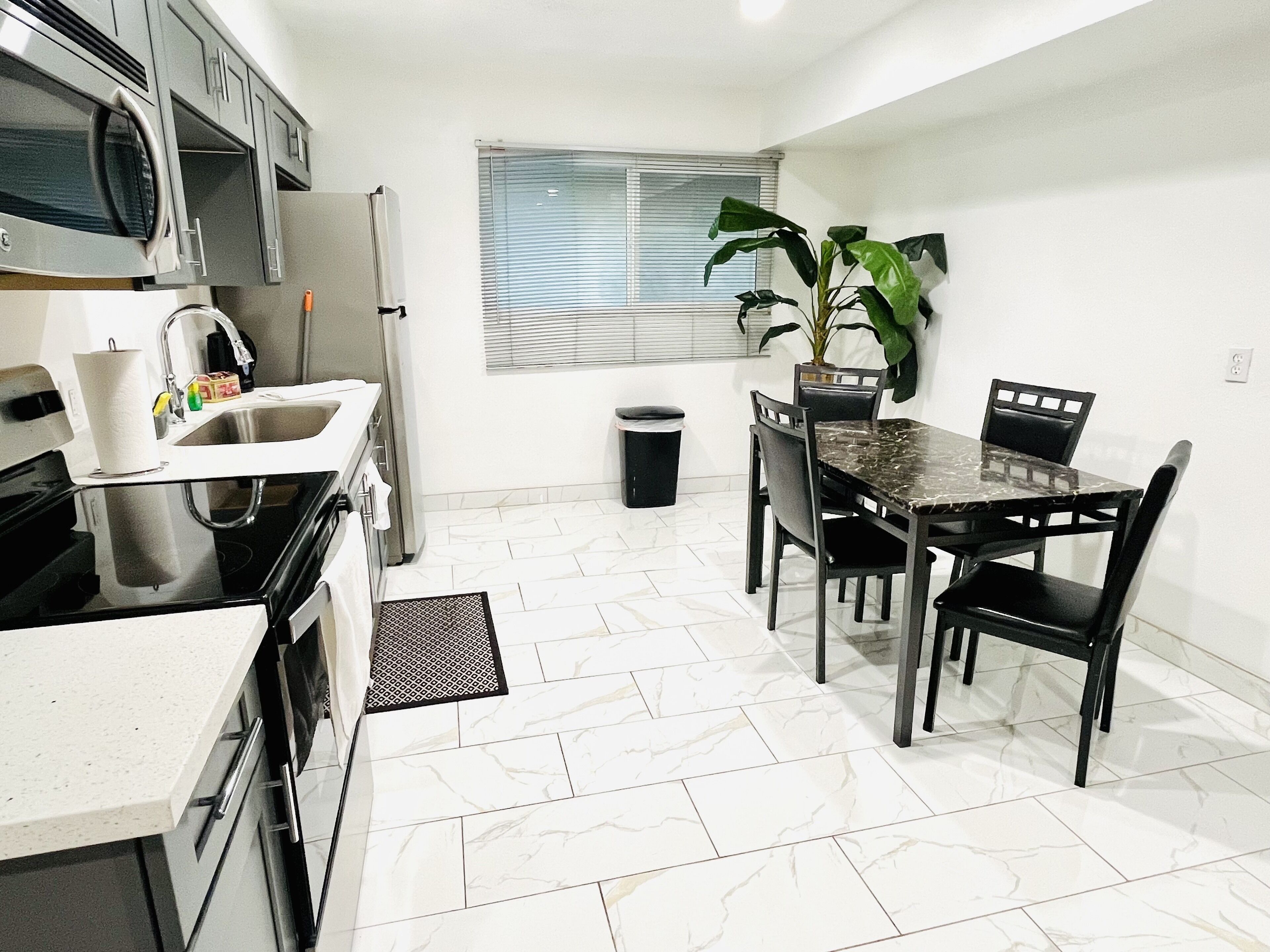 A compact kitchen with a dining area, a microwave, a refrigerator, and a potted plant.