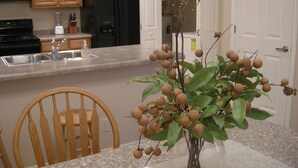 Una cocina con armarios de madera, un refrigerador negro, un lavamanos y una mesa de comedor con un florero de frutas.