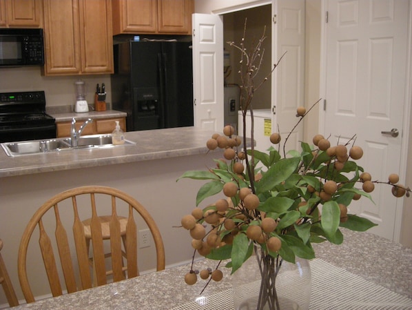 A kitchen with wooden cabinets, a black refrigerator, a sink, and a dining table with a vase of fruit. - Mesquite Nevada Condominium Vacation Rental Ground Level (Mesquite)