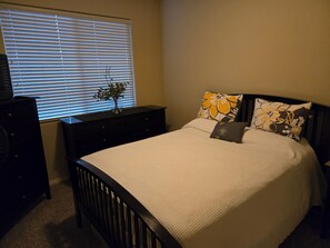 A bedroom with a bed, a dresser, a nightstand, and a window with blinds. - Mesquite Nevada Condominium Vacation Rental Ground Level (Mesquite)