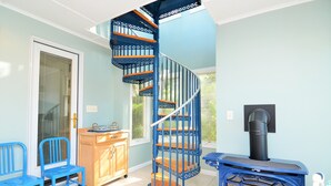 Una habitación con una escalera espiral azul, un aparador de madera, una silla azul y una estufa de leña.