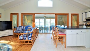 Amplia sala de estar con techo alto, un ventanal grande, televisor, sofá y una zona de cocina con barra.