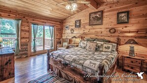 A rustic cabin bedroom with a wooden ceiling, a large bed with a quilt, a ceiling fan, and a view of the outdoors. - Happy Bears Cabin | Beary Cozy Getaway w/ Fireplace & Forest Views (Ruidoso)