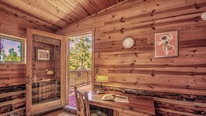 A wooden cabin interior with a door, windows, a clock, a framed picture, and a table with an open book. - Happy Bears Cabin | Beary Cozy Getaway w/ Fireplace & Forest Views (Ruidoso)