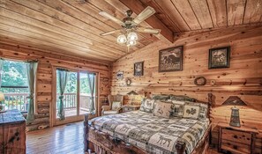 Un dormitorio rústico con techo de madera, una cama grande con colcha y un ventilador de techo, con vista al exterior.