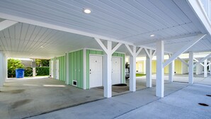 Un área de estacionamiento techada con pilares blancos y paredes verdes, que conduce a habitaciones individuales con puertas blancas.