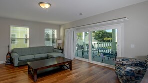 Relax in this inviting living room with a sofa, coffee table, and armchair, leading to a patio with a dining table and outdoor seating.