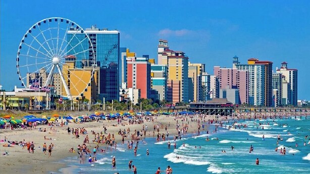 Una playa con una noria y el horizonte de una ciudad al fondo.