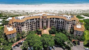 A large, multi-story hotel with a curved roofline, surrounded by lush greenery and a beach view. - Turtle Dunes Oceanfront Ground floor 2br/2ba (Amelia Island)