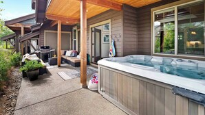Een overdekt terras met een jacuzzi, buitenmeubels en uitzicht op het huis.