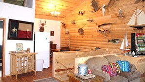 A cozy cabin interior with wooden walls, a dining area, and a living room with a sofa and pillows.