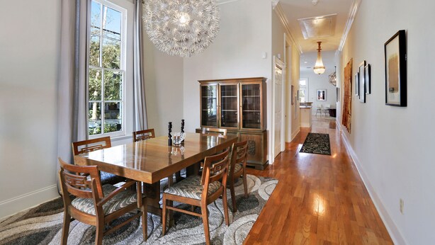 Un comedor con una mesa y sillas de madera, una araña y un aparador con puertas de cristal.