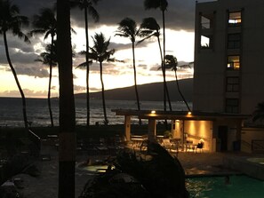 A hotel with a pool, outdoor seating, and a view of the ocean at sunset.
