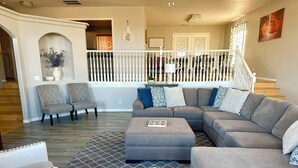 Un salon comprenant un canapé d’angle, deux fauteuils, un tapis à motifs et un escalier avec une rampe.
