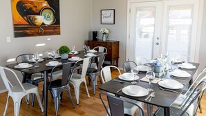 Un coin repas avec une grande table dressée pour six personnes, entourée de chaises modernes, d’une petite plante en pot et d’un bol décoratif.